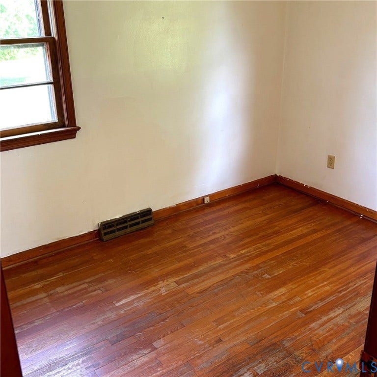 Wood-finish flooring with a natural grain pattern, white walls, and a window with wood trim