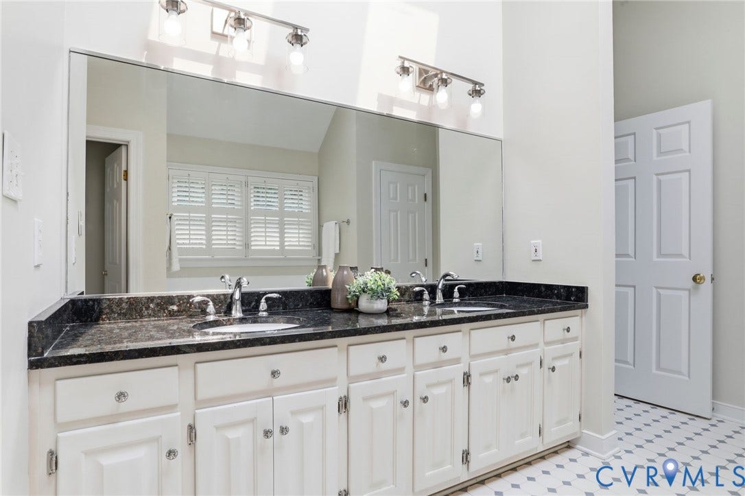 2904 Old Gun Rd W, Old Gun, Midlothian, VA 23113 Dual vanity featuring white cabinetry with silver-toned hardware, a dark countertop, and two undermount sinks with chrome faucets