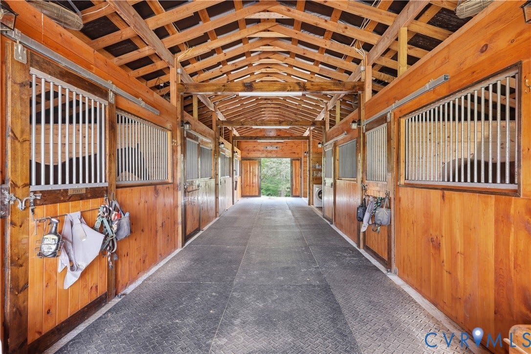 25181 W Soap Stone Rd, Amelia, VA 23083 Barn interior featuring multiple stalls with wood paneling and metal grating, exposed wood beam ceiling, and durable textured flooring