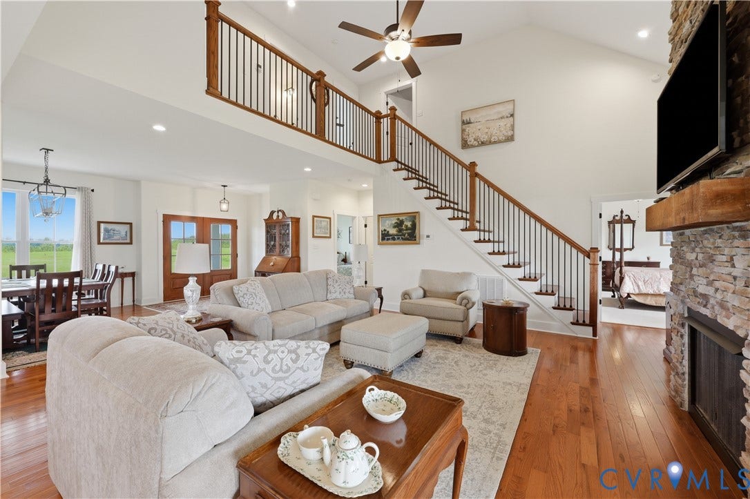 25181 W Soap Stone Rd, Amelia, VA 23083 Two-story living area featuring wood-finish flooring, a stone fireplace with a substantial wood mantel, and a prominent staircase with dark wood handrails and black balusters