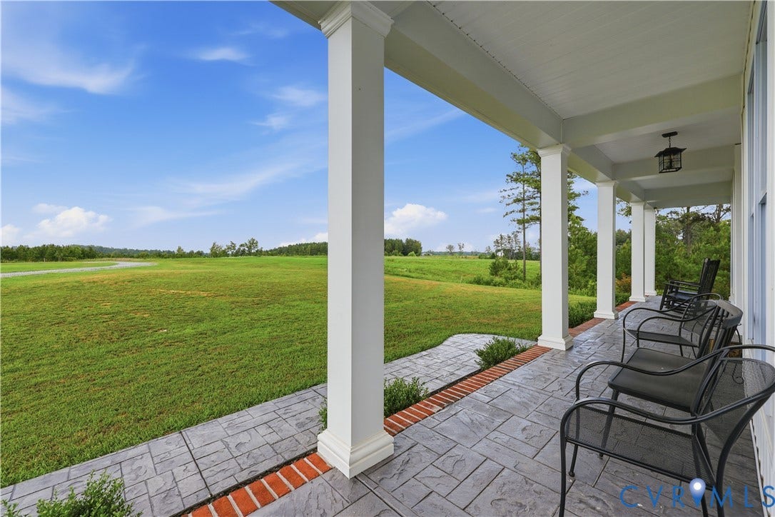 25181 W Soap Stone Rd, Amelia, VA 23083 Expansive covered front porch featuring a stamped concrete surface with brick accents, multiple white columns, and a pendant light fixture