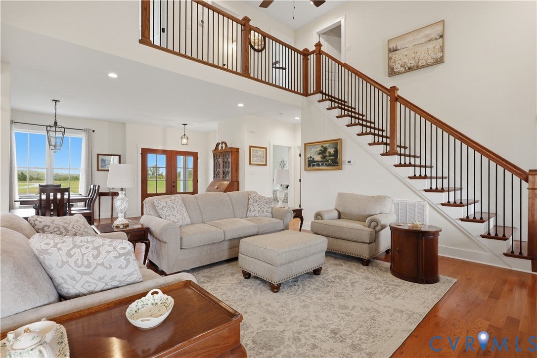 25181 W Soap Stone Rd, Amelia, VA 23083 Spacious living area featuring wood-finish flooring, a grand staircase with dark iron balusters and wood handrails, and an open-concept design