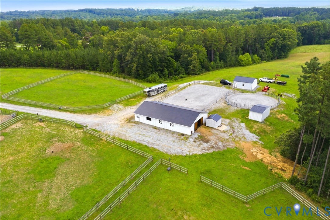 25181 W Soap Stone Rd, Amelia, VA 23083 Expansive property featuring a white barn with a dark roof, multiple fenced green pastures, a gravel riding arena, and additional outbuildings, all surrounded by mature treelines