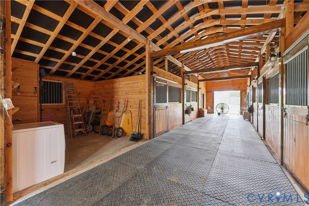 25181 W Soap Stone Rd, Amelia, VA 23083 Wood-paneled barn interior featuring multiple stalls with metal grates, exposed beam ceiling, and durable rubber flooring