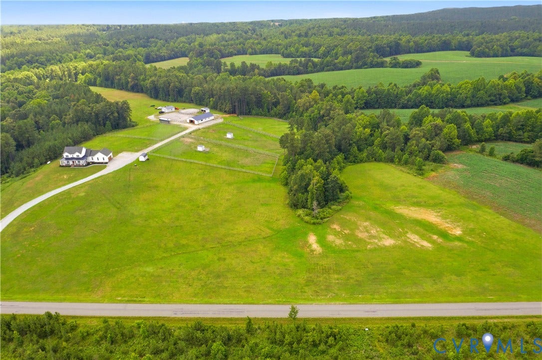 25181 W Soap Stone Rd, Amelia, VA 23083 Expansive rural property featuring a white residence with a wrap-around porch, multiple outbuildings, a long gravel driveway, and extensive green fields bordered by mature trees
