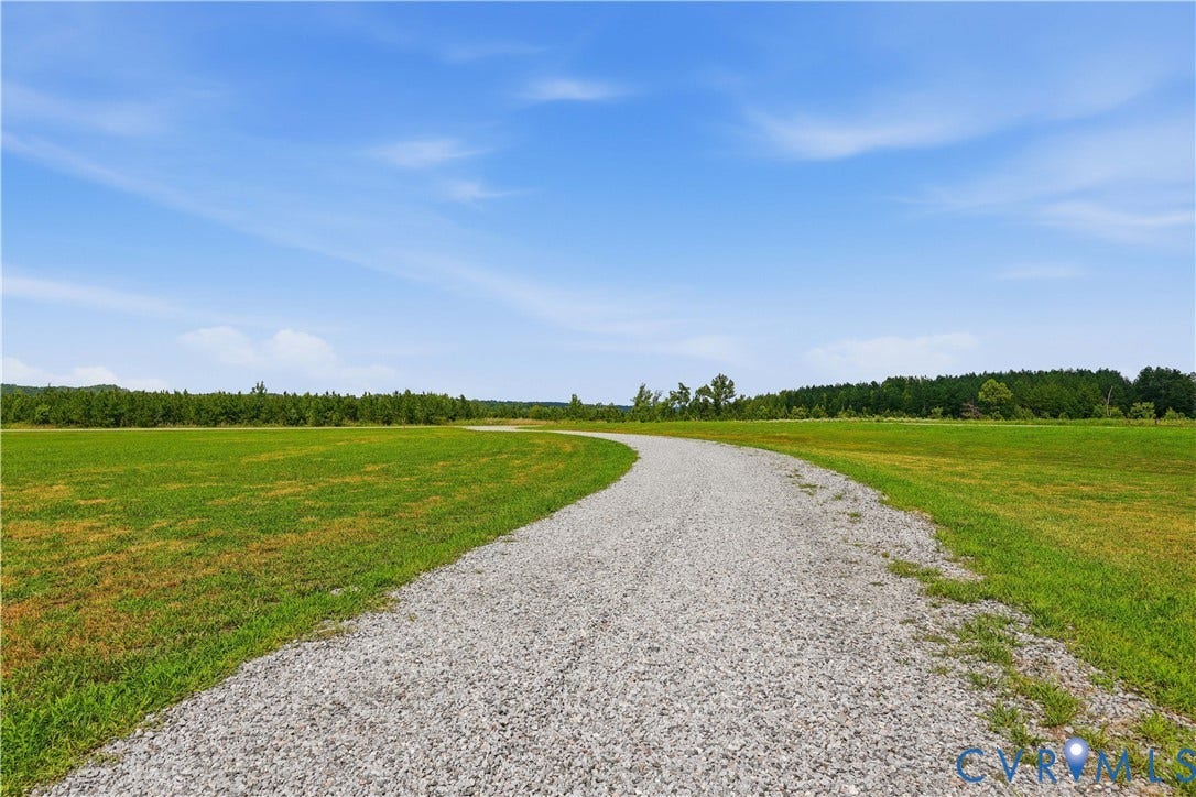 25181 W Soap Stone Rd, Amelia, VA 23083 Winding gravel pathway traversing expansive green fields, bordered by a dense line of trees in the background