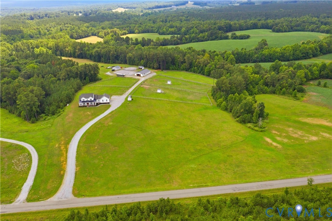 25181 W Soap Stone Rd, Amelia, VA 23083 Expansive property featuring a white residence with a dark roof and a porch, surrounded by lush green fields and mature trees