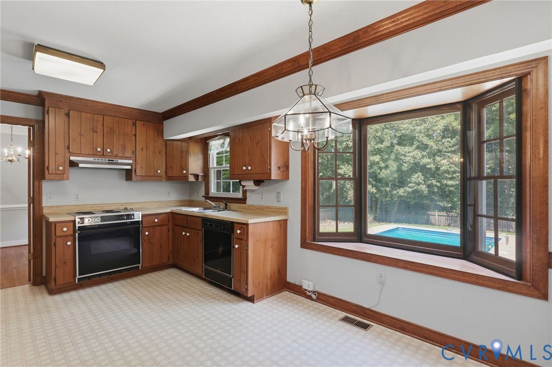 Eat-in kitchen featuring abundant cabinetry, generous counter space, and a large bay window overlooking the backyard and pool.