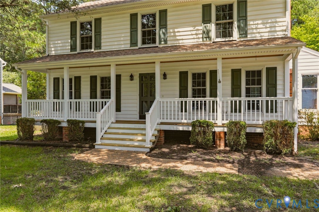 Classic two-story Colonial with a full covered front porch, mature shade trees, and a spacious front yard.