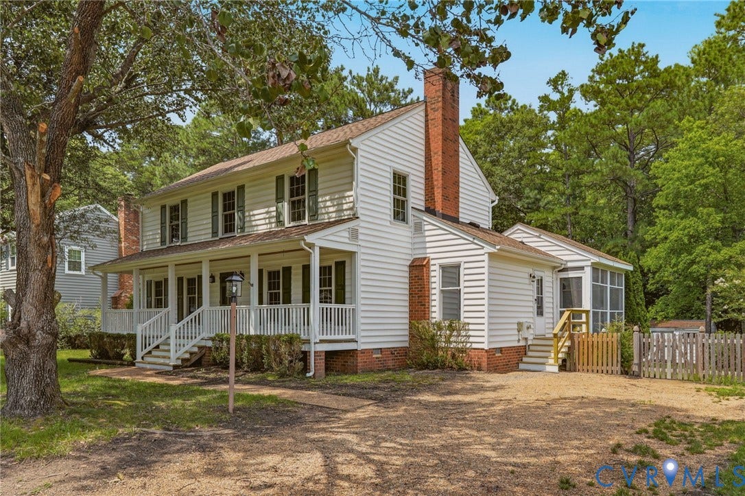 Classic two-story Colonial with a full covered front porch, mature shade trees, and a spacious front yard.