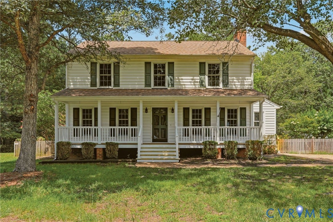 Classic two-story Colonial with a full covered front porch, mature shade trees, and a spacious front yard.
