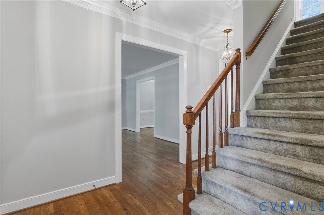 Welcoming foyer with hardwood flooring, a staircase with wood handrail, and an open entry to the main living areas.