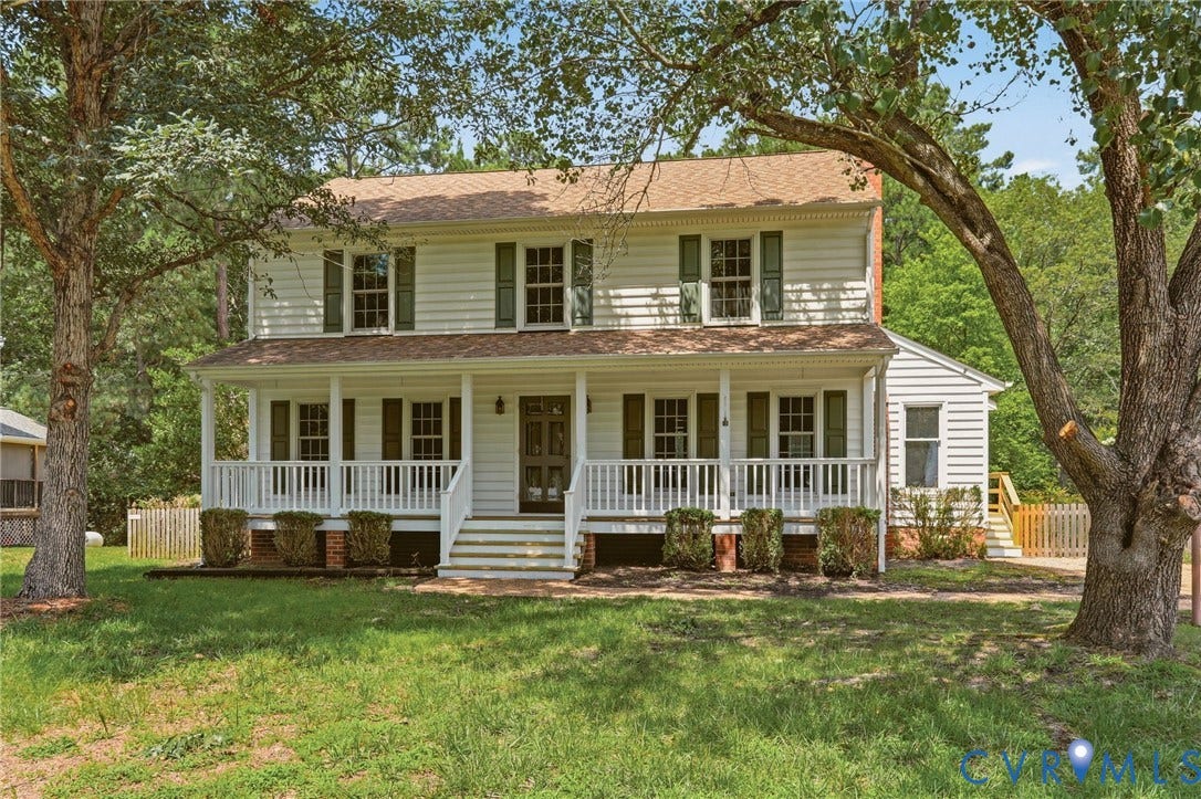Classic two-story Colonial with a full covered front porch, mature shade trees, and a spacious front yard.