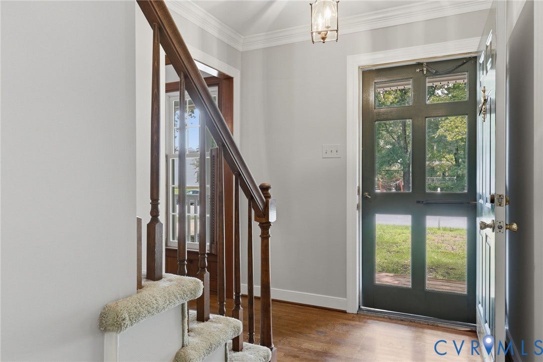 Welcoming foyer with hardwood flooring, a staircase with wood handrail, and an open entry to the main living areas.