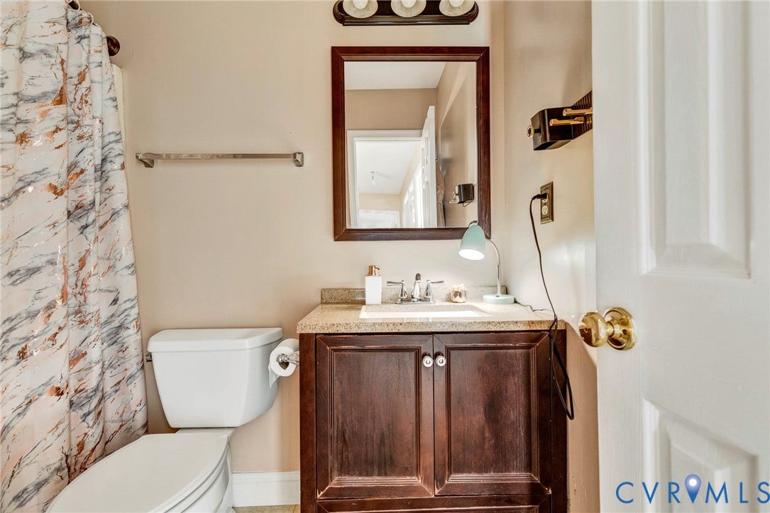 1601 Varina Station Court, Henrico, VA 23231 White toilet, dark wood-finish vanity with a light speckled countertop, framed mirror, and a three-bulb wall-mounted light fixture