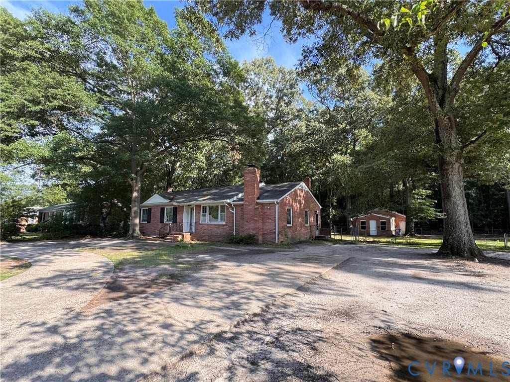 Brick ranch-style home featuring a prominent chimney, dark shutters, and a white front door