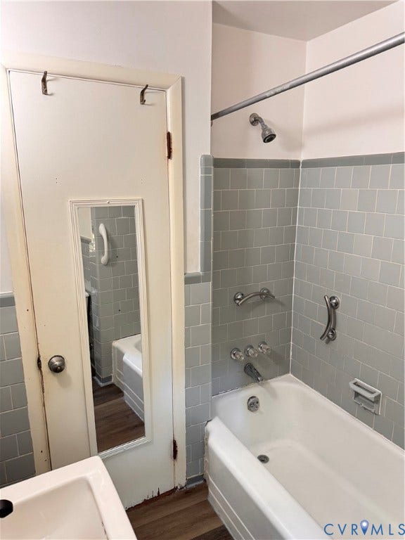 Bathroom featuring light gray tiled shower surround, integrated bathtub, and chrome fixtures