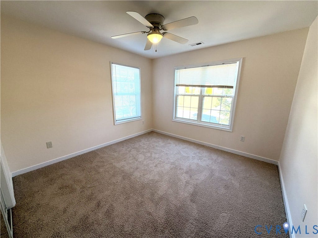 Neutral wall paint with two windows, carpeted flooring, and a ceiling fan with integrated lighting