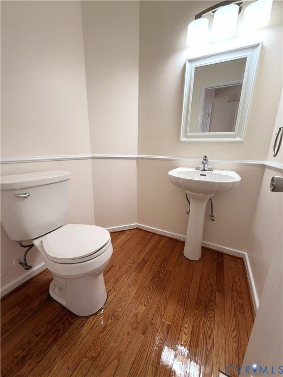 Wood-finish flooring, white pedestal sink, framed mirror, and three-light vanity fixture