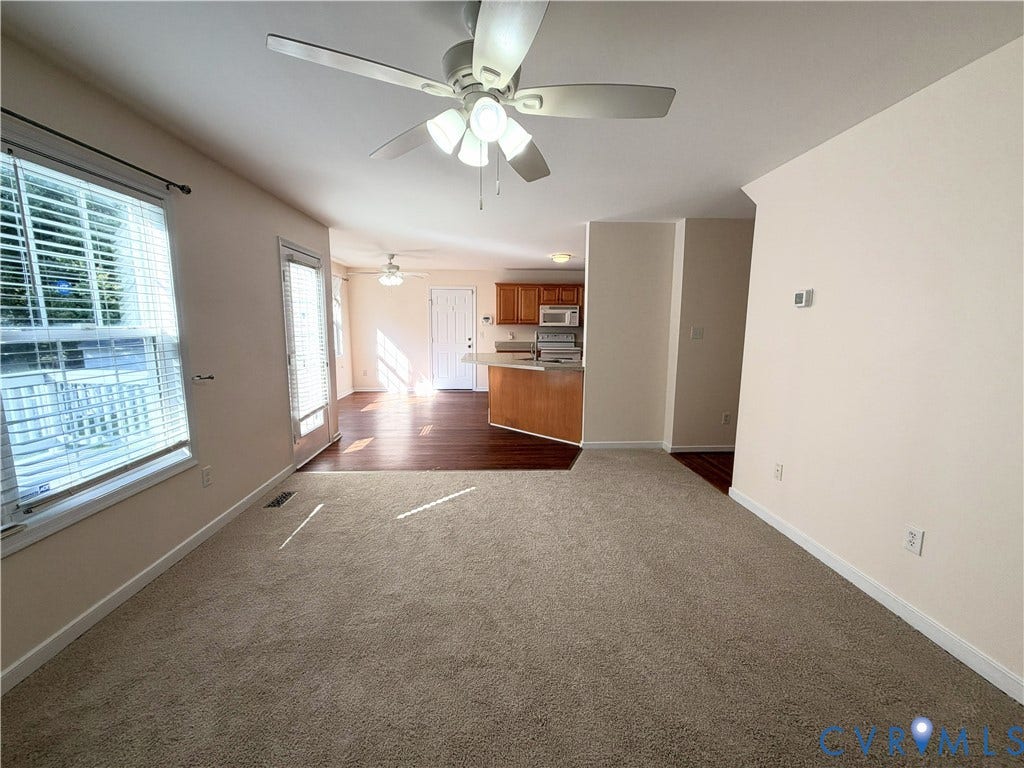 Carpeted living area with a ceiling fan, a large window with blinds, and a glass-paneled exterior door