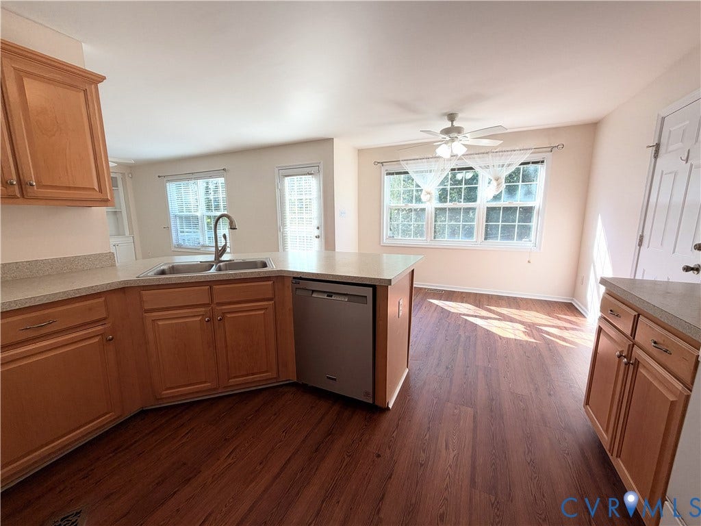 Kitchen featuring wood-finish cabinetry, stainless steel dishwasher, double basin sink with gooseneck faucet, and light-toned countertops