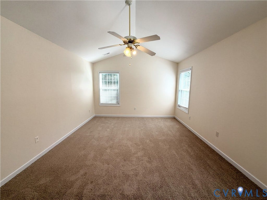Vaulted ceiling with an attached ceiling fan, two windows with blinds, and carpeted flooring