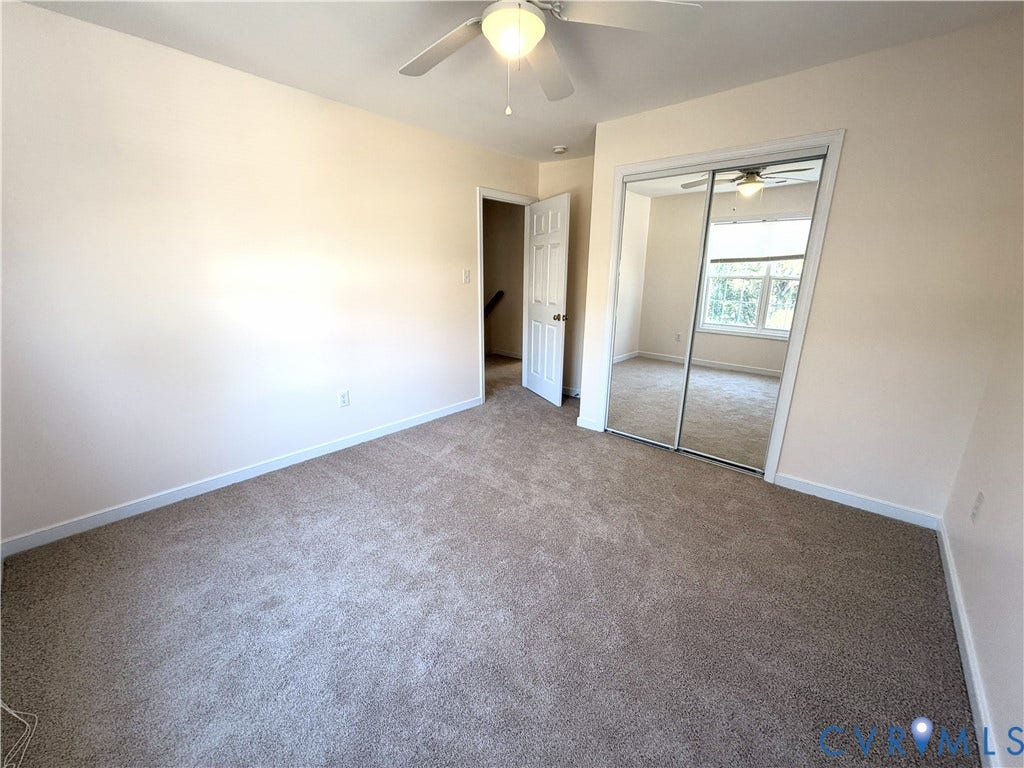 Carpeted room featuring a ceiling fan with integrated lighting, mirrored closet doors, and painted walls