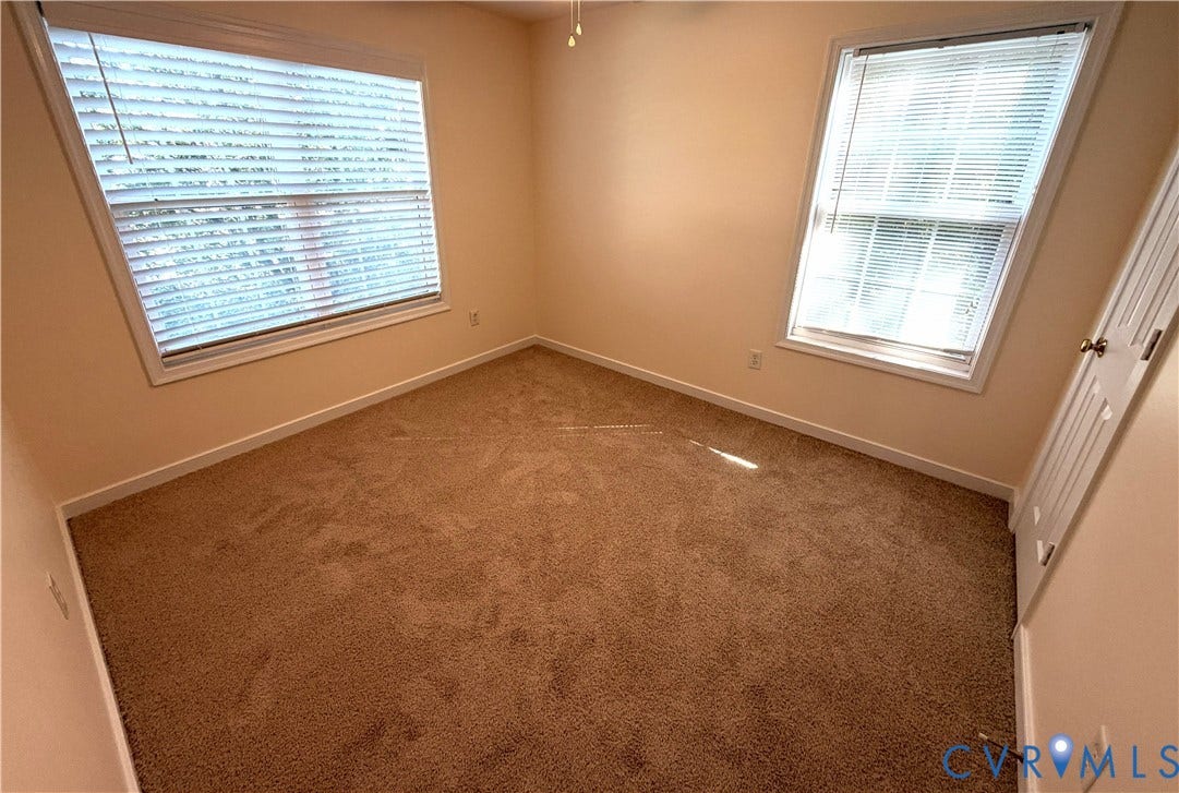 Carpeted flooring, two windows with blinds, white trim, and light-colored walls