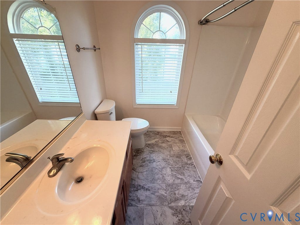 Bathroom featuring an arched window, white bathtub with shower, vanity with integrated sink, and patterned flooring