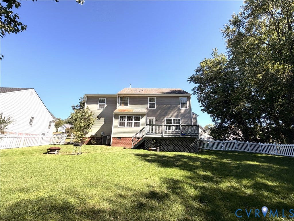 Expansive backyard featuring a manicured lawn, white picket fencing, large mature trees, and a multi-level deck with lattice skirting