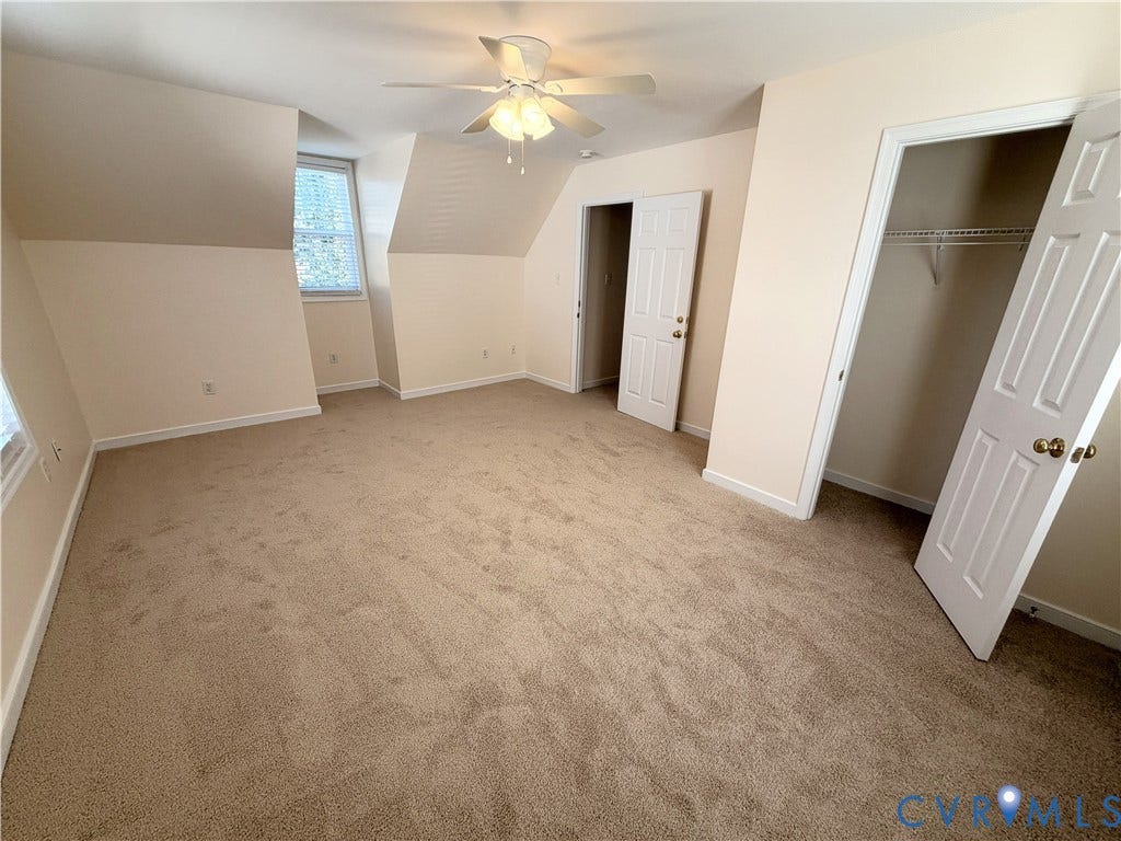 Neutral carpeted flooring, sloped ceiling details, multiple windows with blinds, ceiling fan, and built-in closet with wire shelving