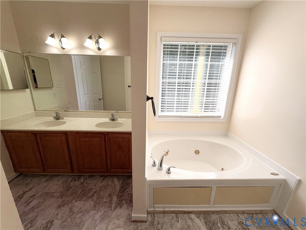 Dual vanity with wood cabinetry and an integrated corner bathtub with a window