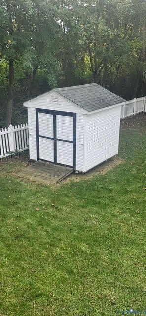 White storage shed with dark trim, asphalt shingle roof, and a wooden ramp