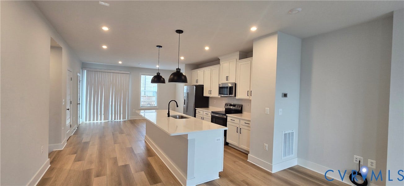 Open-concept living area featuring wood-finish flooring, recessed lighting, and a kitchen island with pendant lighting