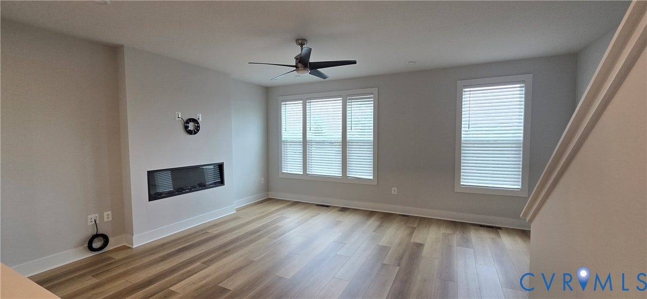 Wood-finish flooring, linear fireplace, multiple windows with blinds, ceiling fan, and crisp white trim