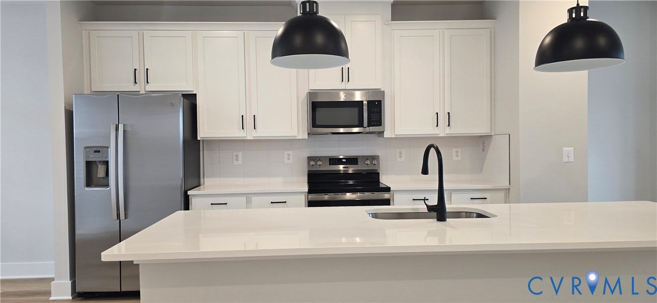 Modern kitchen featuring white shaker cabinetry, stainless steel appliances, a tile backsplash, a large kitchen island with a sink, and pendant lighting