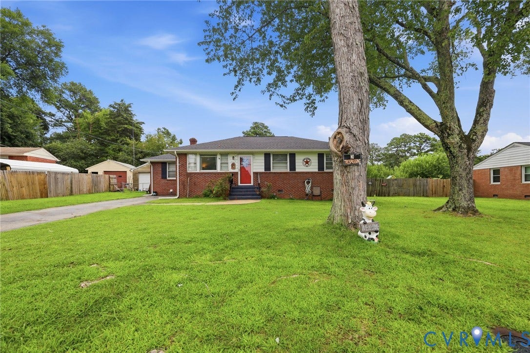 Brick-front home featuring a paved driveway and mature trees