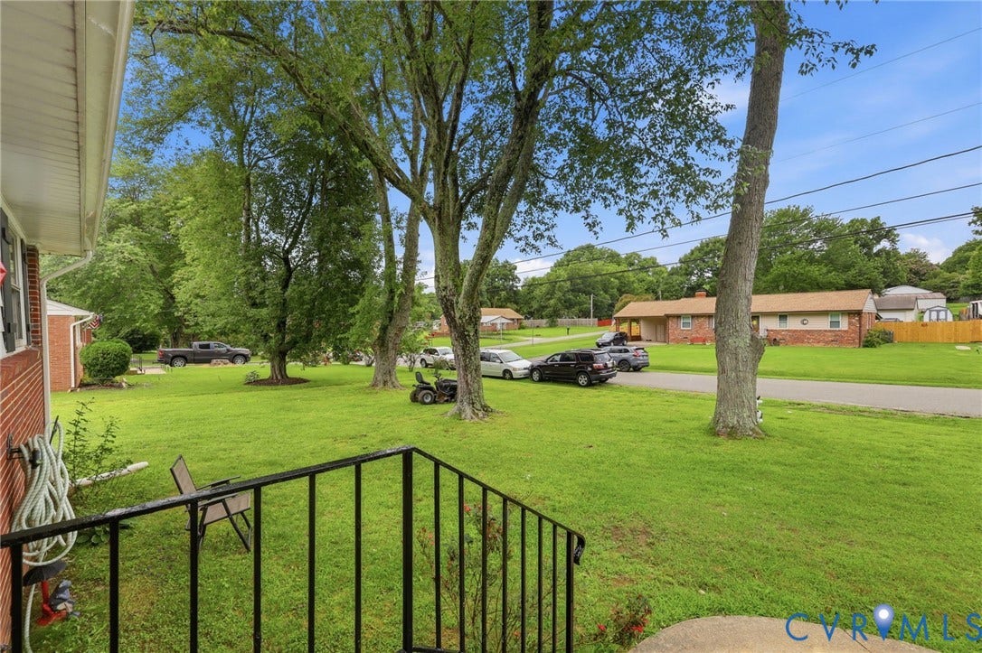 Expansive front lawn with mature shade trees, a red brick exterior, and black porch railing