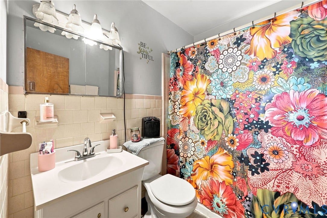 Bathroom featuring a white vanity with integrated sink, coordinating commode, and a shower area