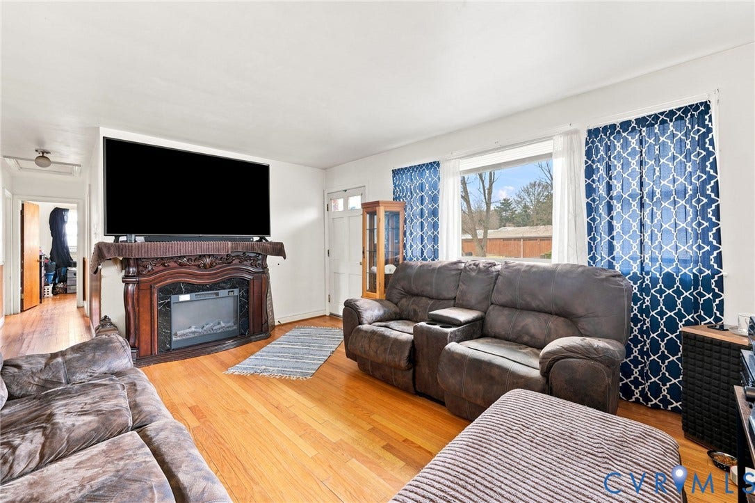 Living area featuring wood-finish flooring, an ornate carved wood fireplace surround with an electric insert, and a white entry door with glass panels
