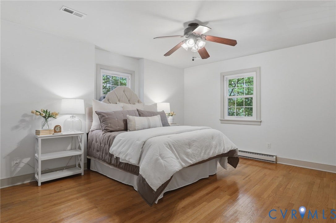 Bedroom featuring wood-finish flooring, two windows with white trim, and a ceiling fan with integrated lighting