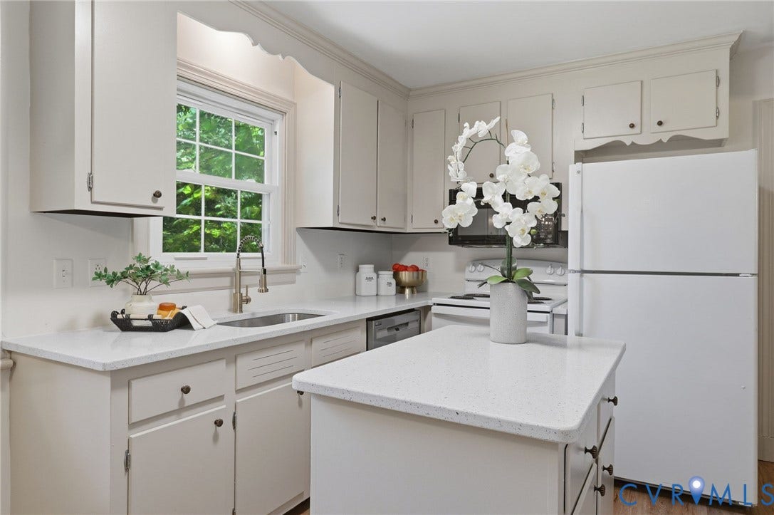 Light-filled kitchen featuring white cabinetry, quartz countertops, a double-basin stainless steel sink with a gooseneck faucet, a built-in dishwasher, and a center island