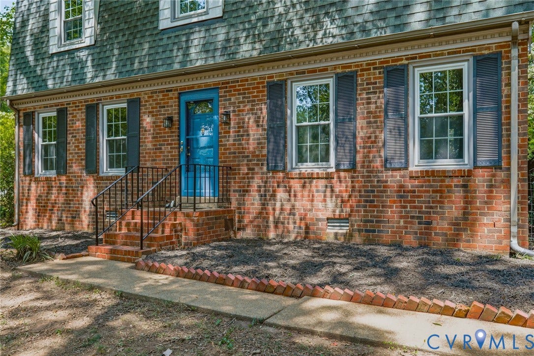 Brick facade residence featuring a blue entry door, dark shutters, and a covered porch with metal railings