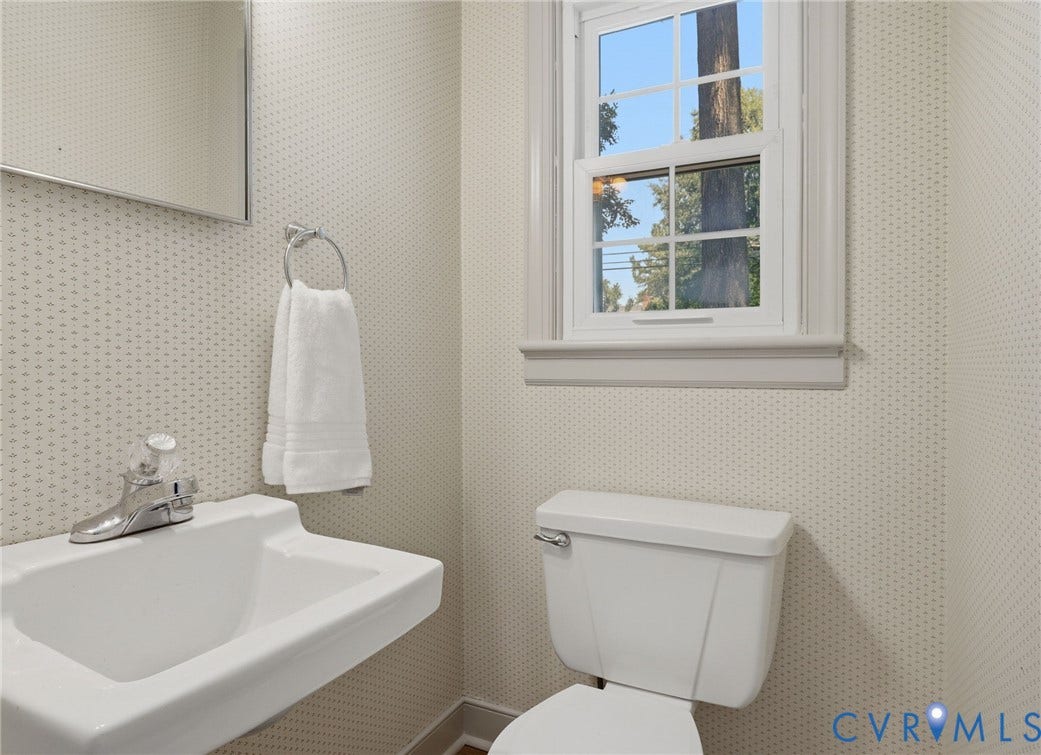 Pedestal sink with chrome faucet, complemented by patterned wallpaper and a double-hung window