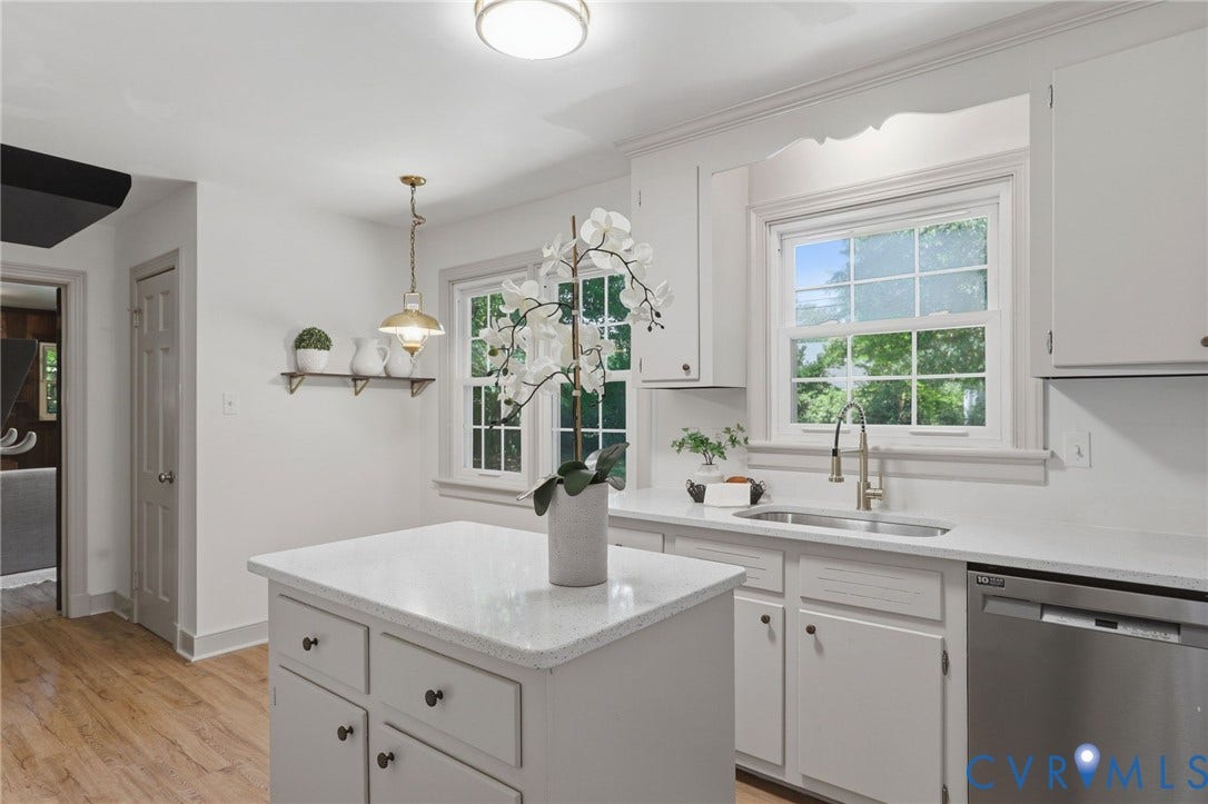 Kitchen featuring white cabinetry, light-toned countertops, a stainless steel dishwasher, and wood-finish flooring