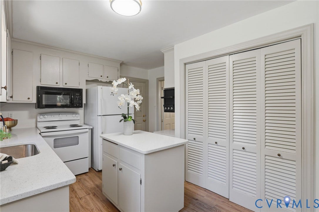 Kitchen featuring white cabinetry, light-toned countertops, a stainless steel sink, wood-finish flooring, and a central island with storage