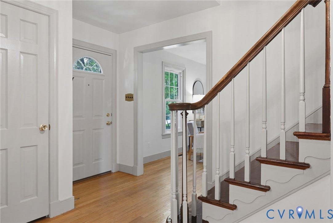 Entryway featuring wood-finish flooring, a white paneled door with an arched transom window, and a staircase with a wood banister and white balusters