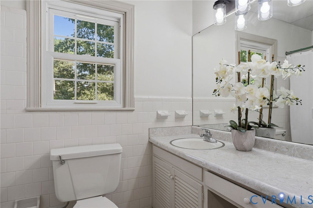 Bathroom featuring a window with grid panes, white wall tiling, a vanity with a laminate countertop, an integrated sink, and a large wall mirror