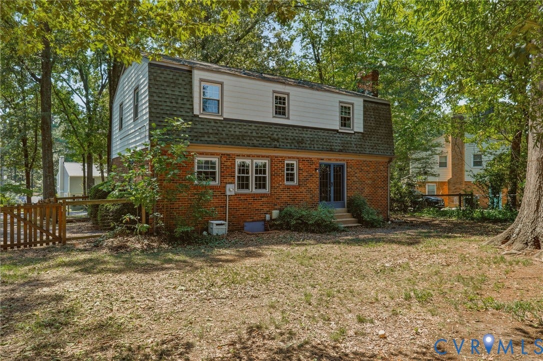 Brick-clad exterior with a gambrel roofline and dormer windows, featuring a ground-level patio door and a fenced side yard