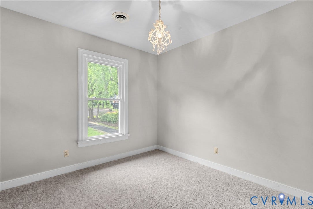 Bright room featuring a single window, a crystal chandelier, and light gray carpeting